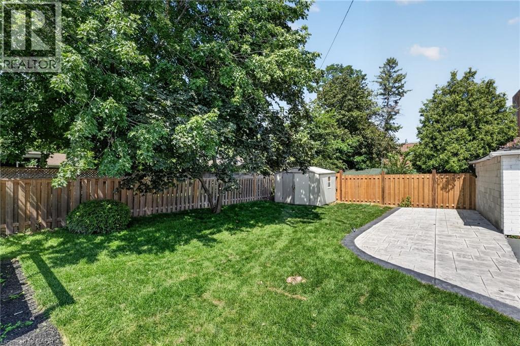 Expansive backyard featuring a manicured lawn, a large shade tree, a decorative paved patio, and perimeter fencing - 43 E Brucedale Avenue E, Hamilton, ON