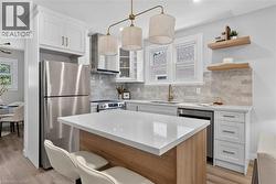 Kitchen featuring wood-finish flooring, white cabinetry with gold-tone hardware, stainless steel appliances, a center island with a white countertop, and a tiled backsplash -