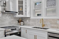 Modern kitchen featuring white cabinetry with brass-finish hardware, stainless steel appliances, and a double-basin sink with a brass-finish faucet -