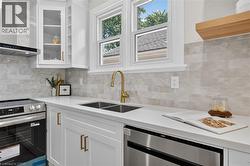 White cabinetry with gold-tone hardware, stainless steel appliances, dual basin sink with a gold-tone faucet, and light-toned tile backsplash -
