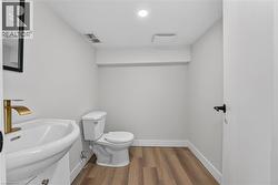 Wood-finish flooring, modern pedestal sink, gold-finish faucet, and recessed lighting -