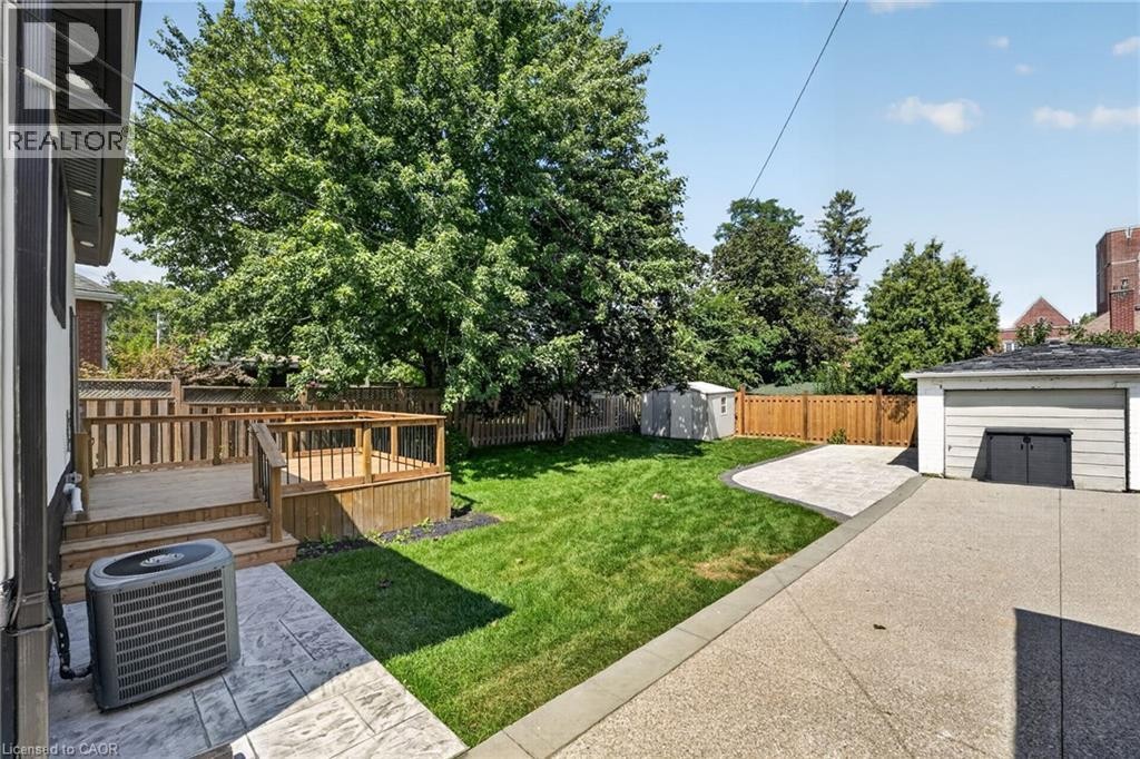 Expansive backyard featuring a multi-level wood deck, manicured lawn, concrete patio, and detached garage - 43 Brucedale Avenue E, Hamilton, ON