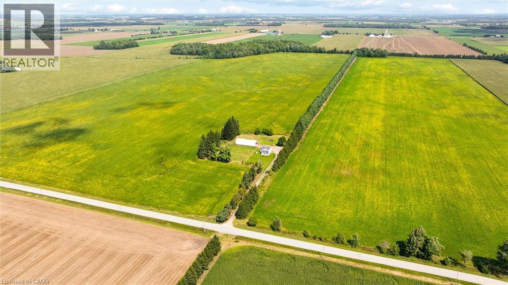 Expansive green fields with a visible residential structure, bordered by a paved road - 5480 Line 42 Line, Mitchell, ON