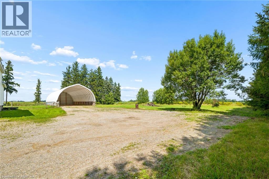Spacious gravel drive with open-sided storage structure, surrounded by mature trees and expansive grass areas - 5480 Line 42 Line, Mitchell, ON