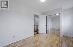 Light-toned wood-finish flooring, white walls, ceiling-mounted light fixture, and a closet with mirrored sliding doors - 