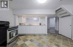 Tile flooring, white cabinetry, stainless steel range, built-in sink, and staircase with storage - 