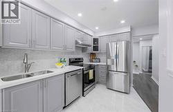 Modern kitchen featuring light gray cabinetry, stainless steel appliances, a double basin sink, white countertops, and a hexagon tile backsplash - 