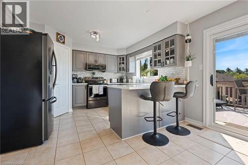 Kitchen featuring gray cabinetry, a white subway tile backsplash, a center island with seating, a stainless steel sink, and tile flooring - 260 Granite Hill Road, Cambridge, ON 