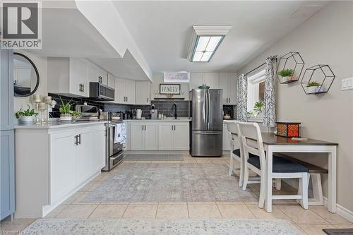 White cabinetry with black hardware, stainless steel appliances, dark subway tile backsplash, light-toned tiled flooring, and a large flush-mount ceiling light - 260 Granite Hill Road, Cambridge, ON 