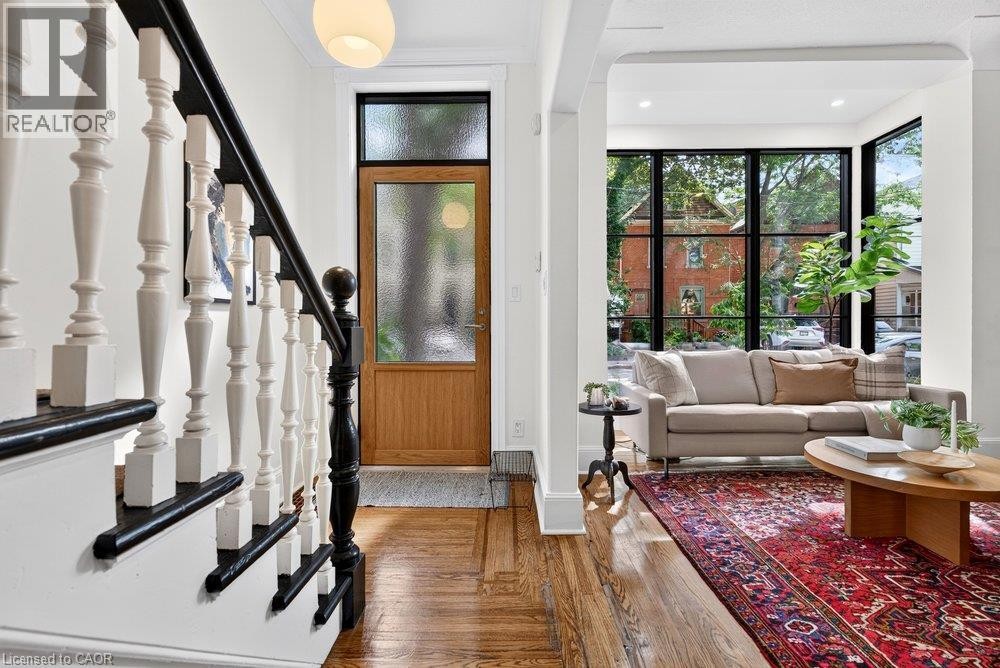 Hardwood flooring throughout, a wood-paneled entry door with frosted glass, and a staircase with white balusters and a dark handrail - 16 Bruce Street, Hamilton, ON