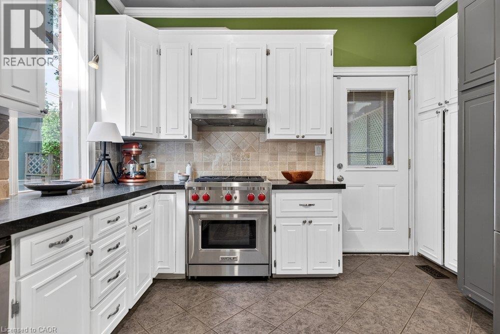 White cabinetry with dark countertops, stainless steel range and hood, tiled backsplash, and patterned floor tiles - 16 Bruce Street, Hamilton, ON