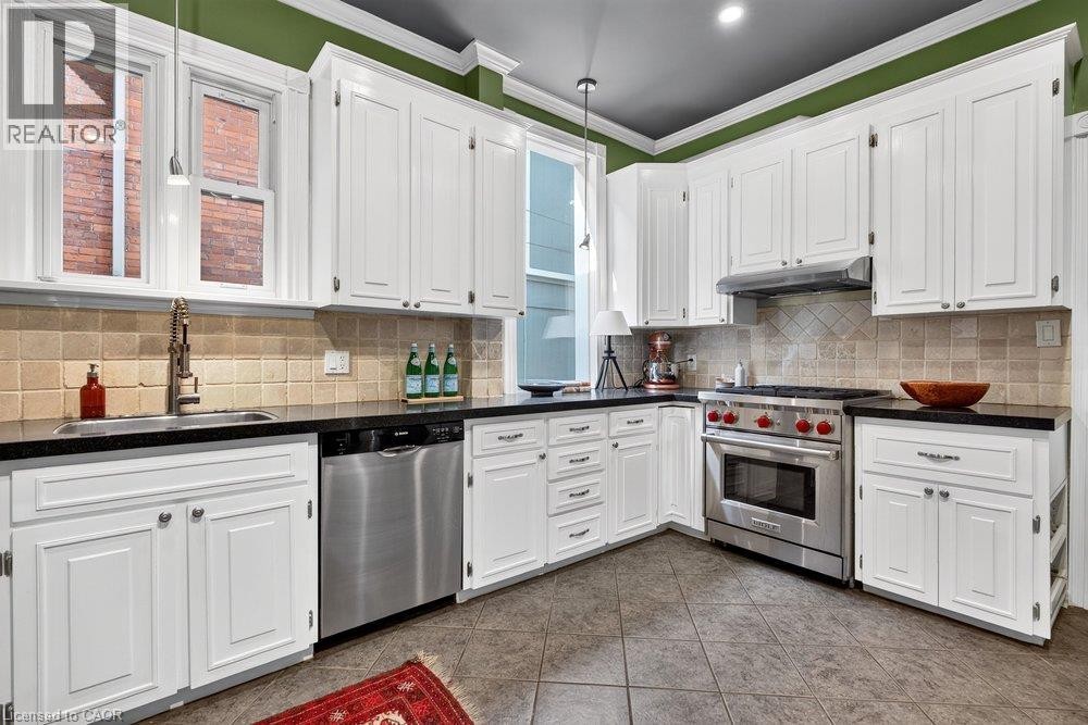 White cabinetry, dark countertops, stainless steel appliances, tile flooring, and a tile backsplash - 16 Bruce Street, Hamilton, ON