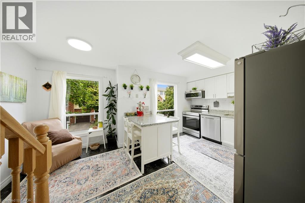 Contemporary kitchen featuring white cabinetry, stainless steel appliances, a center island with seating, and light-colored countertops - 384 Limeridge Road E Unit# 16, Hamilton, ON