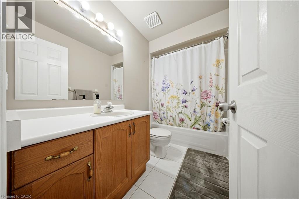 Bathroom featuring a wood-finish vanity with a white countertop, an integrated sink, a large wall mirror, and a white tiled floor - 384 Limeridge Road E Unit# 16, Hamilton, ON