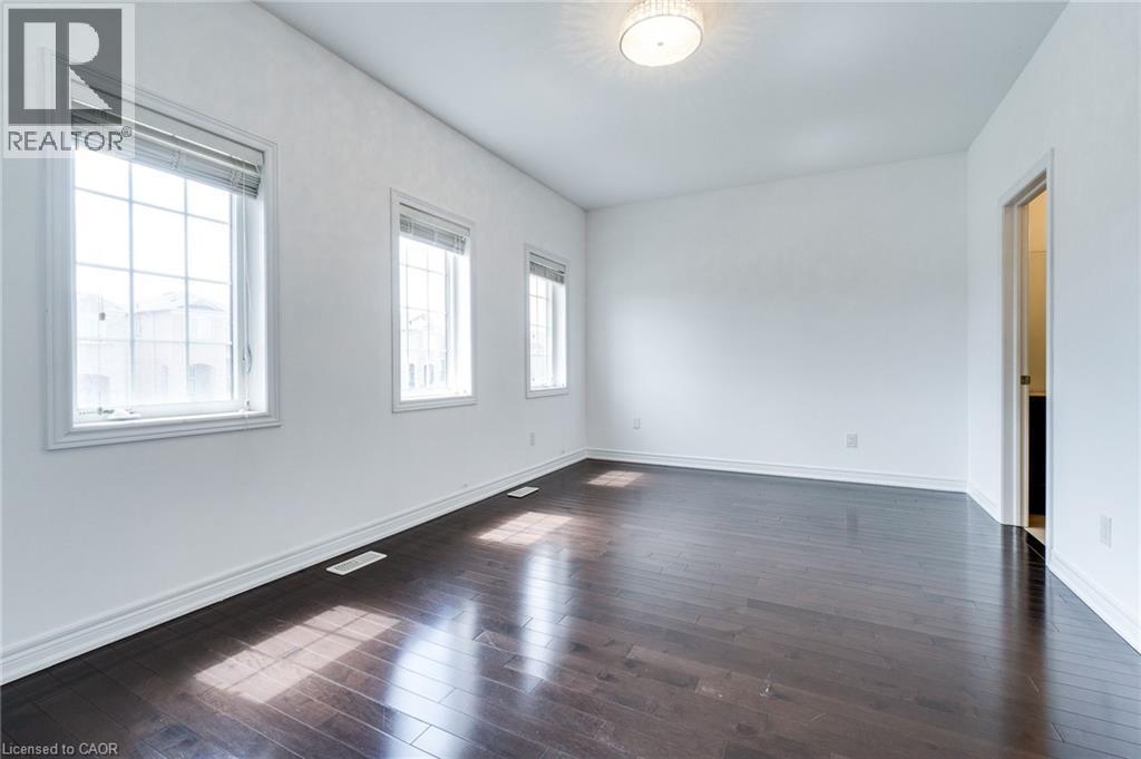 Spacious room featuring dark wood-finish flooring, white walls, multiple windows, and a flush mount ceiling light - 2 Hawstone Road, Vellore, ON