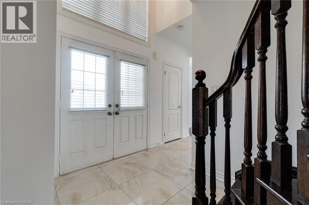 Double entry doors with glass panels, light-toned tiled flooring, dark wood-finish staircase with turned balusters, and a transom window above the entry - 2 Hawstone Road, Vellore, ON