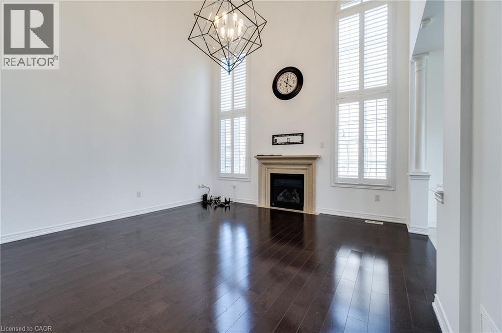 High ceilings with a geometric chandelier, wood-finish flooring, a fireplace with a stone mantel, and tall windows with plantation shutters - 2 Hawstone Road, Vellore, ON