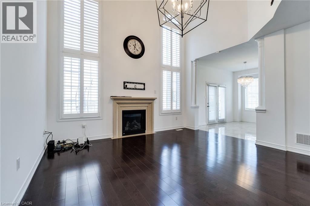 Two-story windows with plantation shutters, dark wood-finish flooring, a fireplace with a stone mantel, a geometric light fixture, and architectural columns - 2 Hawstone Road, Vellore, ON