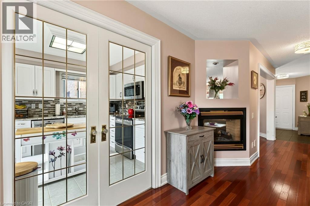 Hardwood flooring, gas fireplace, white French doors with glass panes, kitchen with white cabinetry, and a tile backsplash - 31 Grindstone Way, Hamilton, ON
