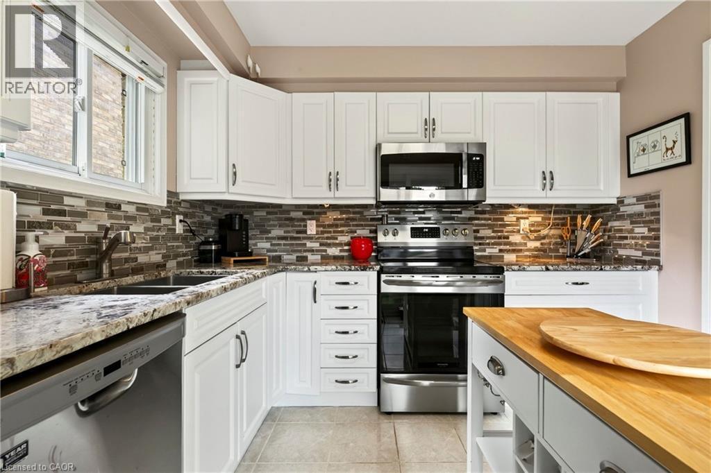 White shaker-style cabinetry, stainless steel appliances, a mosaic tile backsplash, a double basin sink, and wood-finish flooring - 31 Grindstone Way, Hamilton, ON