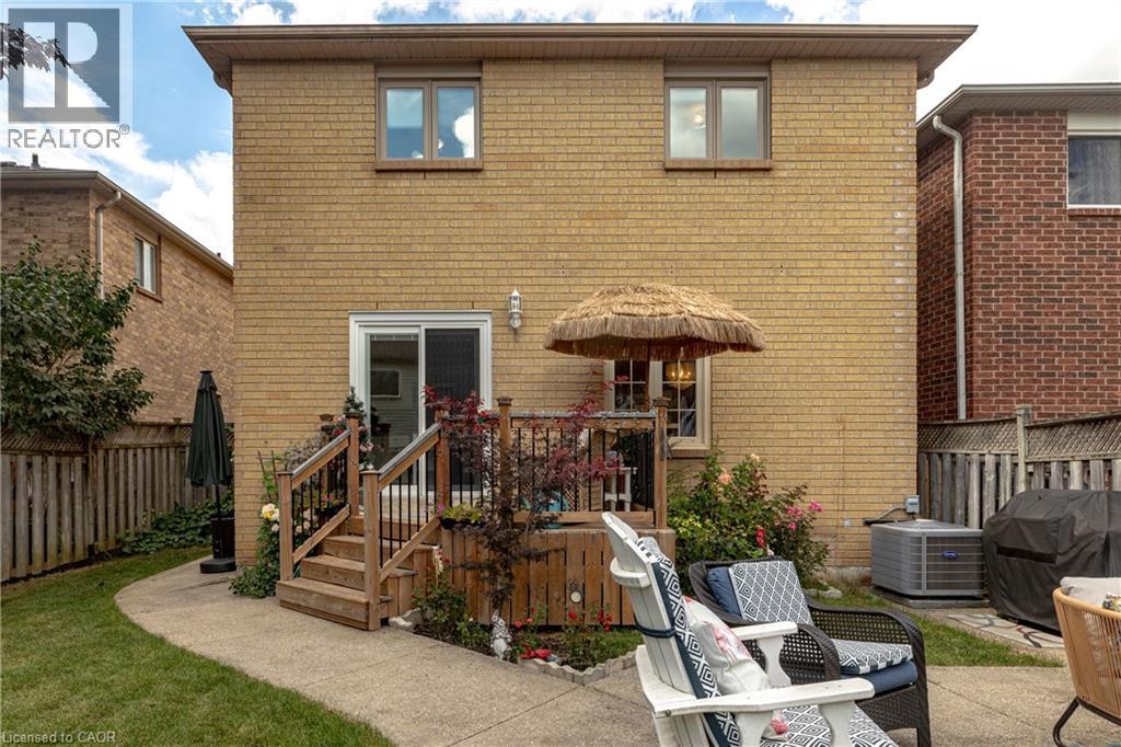 Brick exterior with upper-level windows, ground-level sliding glass door, wooden deck, and concrete patio - 31 Grindstone Way, Hamilton, ON