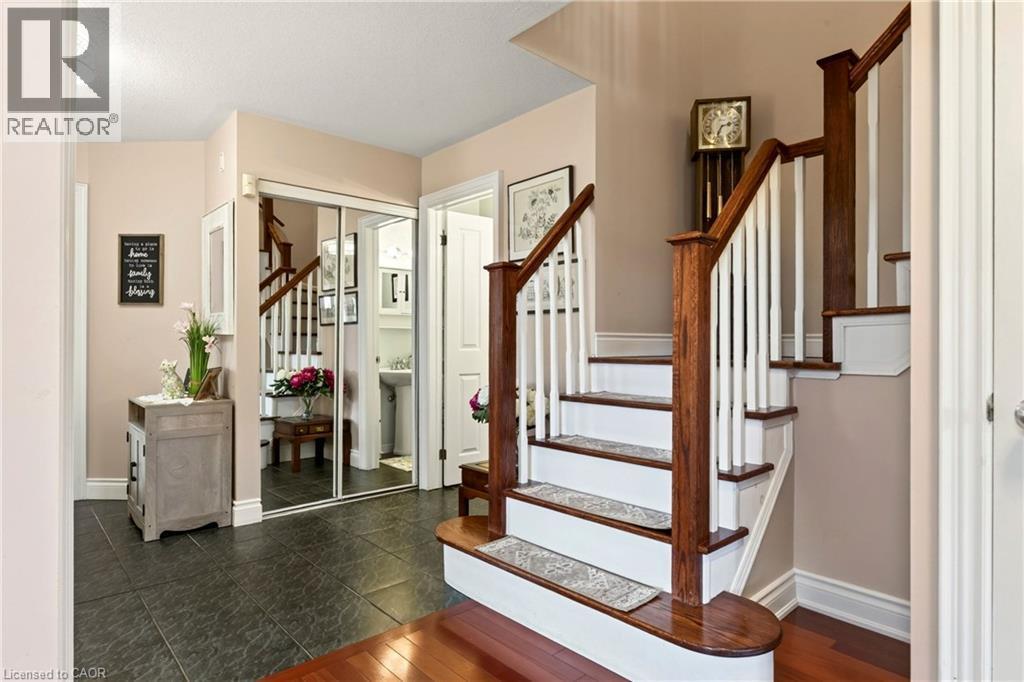 Hardwood staircase with white risers and balusters, dark wood newel posts and handrails, dark tile flooring, and mirrored closet doors - 31 Grindstone Way, Hamilton, ON