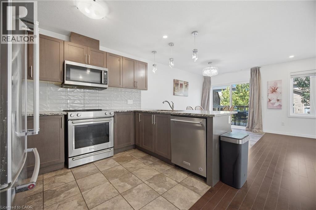Modern kitchen featuring stainless steel appliances, wood-finish cabinetry, a tile backsplash, and a breakfast bar with pendant lighting - 135 Hardcastle Drive Unit# 85, Cambridge, ON