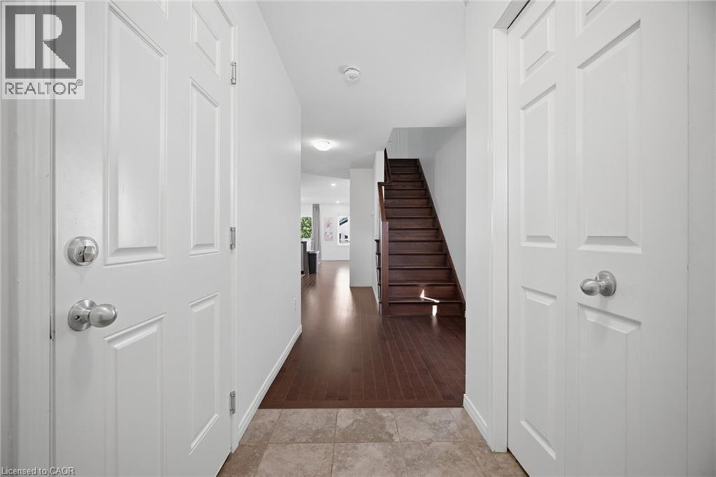 Entryway featuring light-toned tile flooring, white paneled doors with chrome hardware, wood-finish flooring extending into interior spaces, and a dark wood staircase - 135 Hardcastle Drive Unit# 85, Cambridge, ON