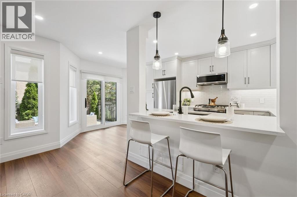 White kitchen cabinetry with stainless steel appliances, a white tile backsplash, and a breakfast bar with pendant lighting - 2294 Seton Crescent, Burlington, ON
