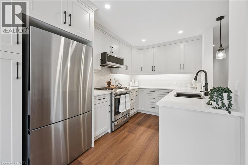 Modern kitchen with white cabinetry, stainless steel appliances, wood-finish flooring, white subway tile backsplash, and a black matte faucet - 2294 Seton Crescent, Burlington, ON