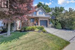 Brick and siding exterior with an attached garage, paver driveway, and mature landscaping - 