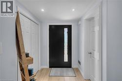 Recessed ceiling lighting, wood-finish flooring, white trim, a solid black entry door with a vertical window, and a white paneled door - 