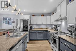 Kitchen featuring a stainless steel double basin sink, stainless steel appliances, wood-finish flooring, two-tone cabinetry, and recessed lighting - 