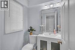 Vanity with integrated sink, rectangular mirror with an etched border, wall-mounted light fixture, white toilet, and window with horizontal blinds - 