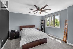 Neutral-toned wall paint with a contrasting accent wall, ceiling fan with integrated lighting, window with exterior foliage, and carpet flooring - 