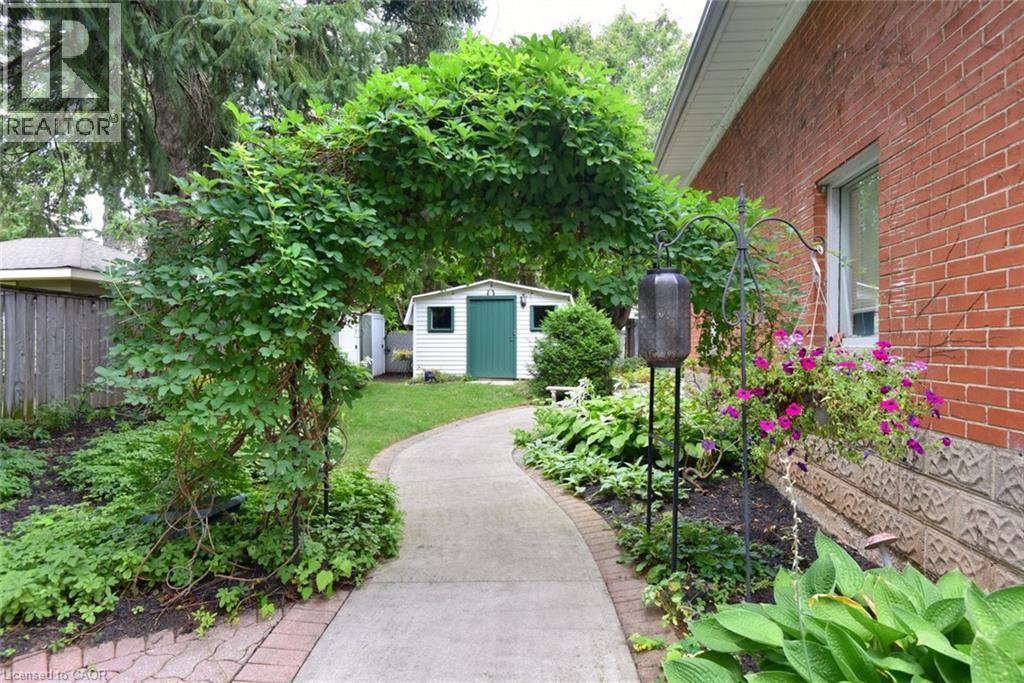 Arched garden trellis, concrete pathway, red brick exterior, landscaped garden beds, and a white storage shed with a green door - 936 Boothman Avenue, Burlington, ON