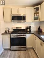 Kitchen featuring a stainless steel range, coordinating microwave, white subway tile backsplash, dark countertops, and wood-finish flooring - 