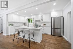 Bright kitchen featuring white shaker cabinetry, stainless steel appliances, a center island with countertop seating, wood-finish flooring, and recessed lighting - 