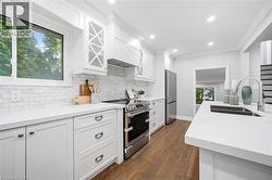Kitchen featuring white cabinetry, light countertops, wood-finish flooring, stainless steel appliances, and a tile backsplash - 
