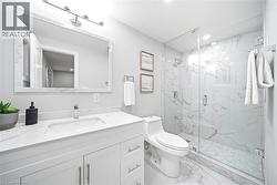 Vanity with an integrated sink and chrome faucet, large framed mirror with overhead lighting, glass-enclosed shower with a tiled bench, and white tile flooring - 