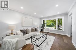Bright, naturally lit living space featuring recessed ceiling lighting, wood-finish flooring throughout, and expansive multi-pane windows framing mature greenery - 