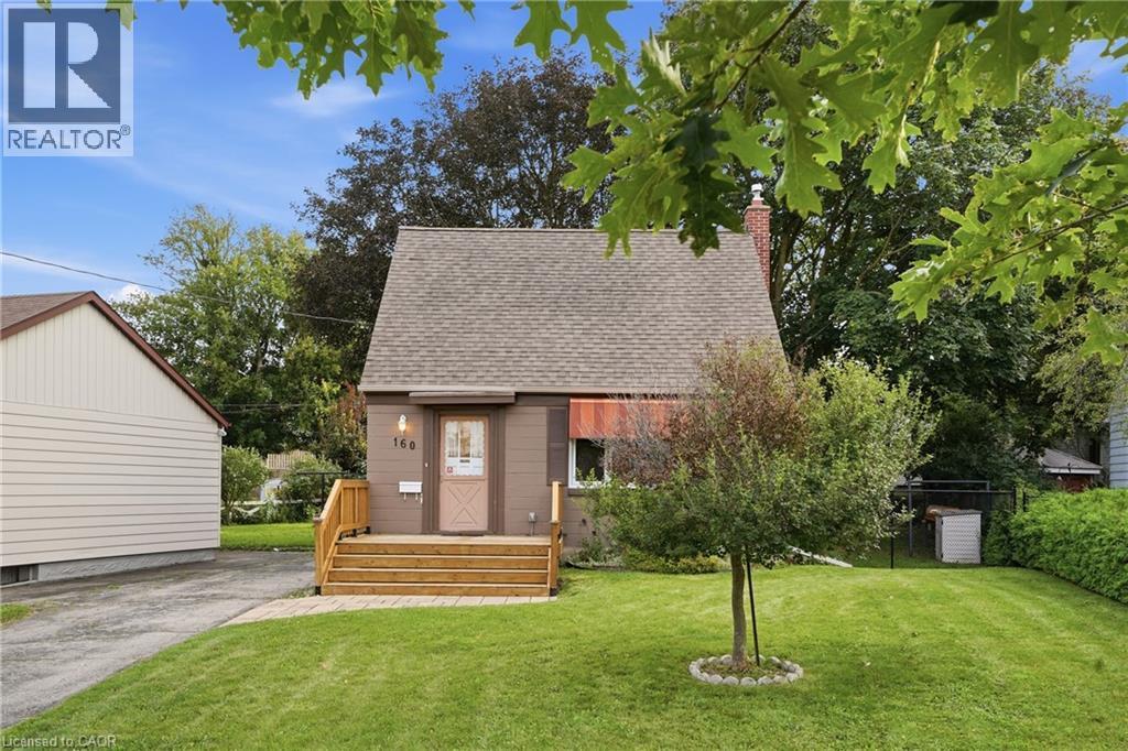 Gable roofline, exterior siding in a neutral tone, front entry with wood steps, mature front yard landscaping, and paved driveway - 160 Lorne Crescent, Kitchener, ON