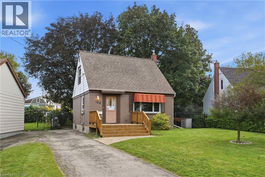Gabled roofline, front entry with wood steps, red and white striped window awning, paved driveway, and established green lawn - 160 Lorne Crescent, Kitchener, ON