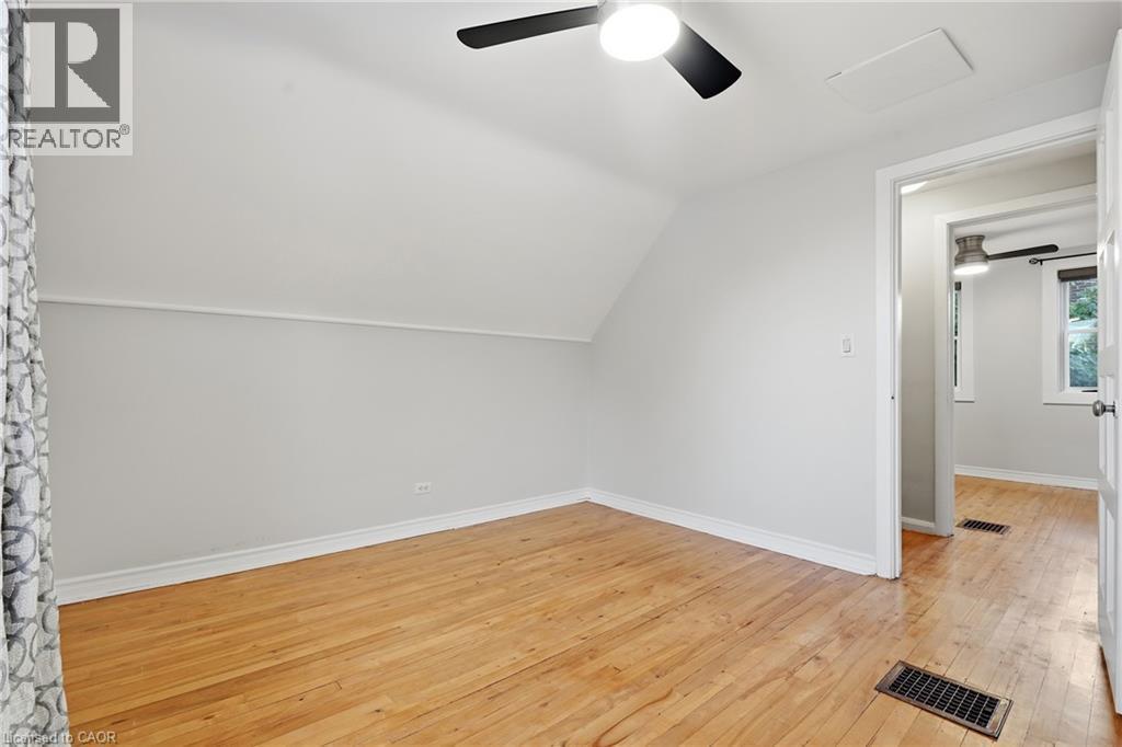 Sloped ceiling room featuring wood-finish flooring, ceiling fan with integrated lighting, and a white paneled door - 160 Lorne Crescent, Kitchener, ON