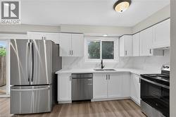 Modern kitchen featuring wood-finish flooring, white cabinetry with matte black hardware, stainless steel appliances, and white countertops with a matching backsplash - 
