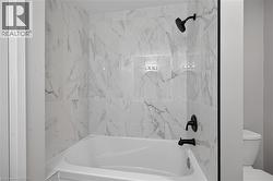 Bathtub with white marble-look wall tiling, matte black showerhead, and matte black tub faucet - 