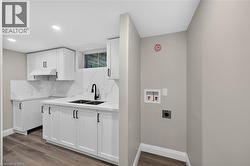 White shaker cabinetry, dark wood-finish flooring, undermount double-basin sink with matte black faucet, and white countertops with integrated backsplash - 