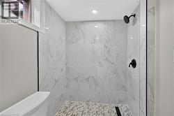 Walk-in shower featuring marble-look tile, a pebble-finish floor, and matte black fixtures - 
