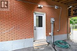 Brick exterior with a white entry door, exterior lighting fixture, and exposed electrical conduit - 