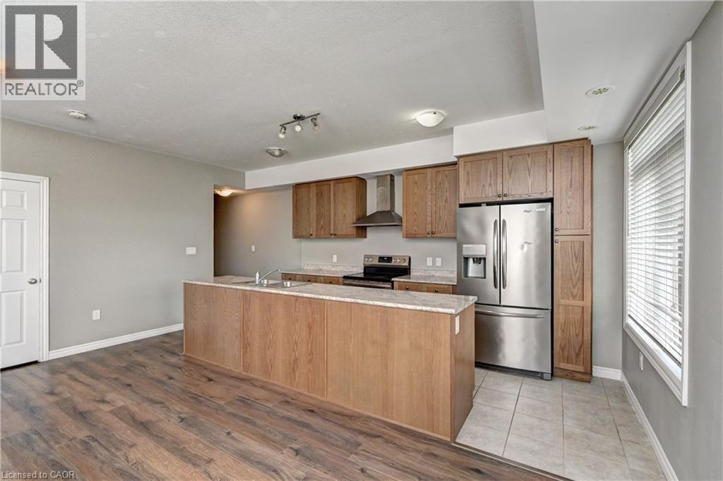 Modern kitchen featuring wood-finish cabinetry, stainless steel appliances including a refrigerator and range hood, granite countertops, and a spacious island with seating - 102 Wheat Lane, Kitchener, ON